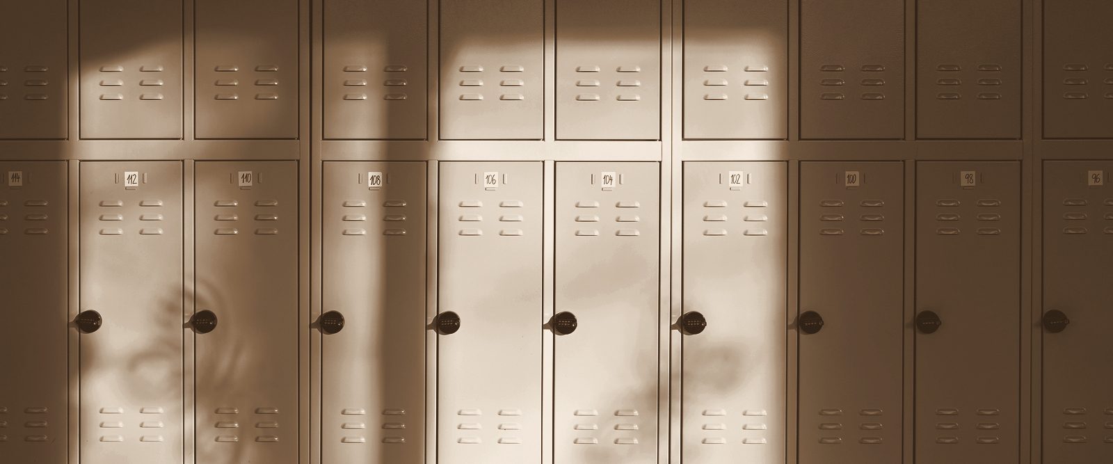 An empty school hallway with sunlight falling across the lockers, in warm bronze